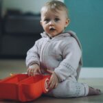 toddler sitting on ground while holding red plastic case