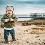 a young boy standing on top of a sandy beach